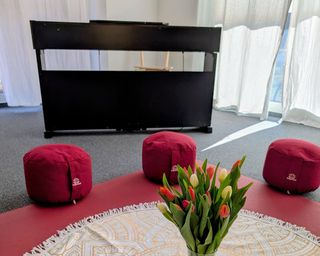 Meditationskissen im Kreis um ein Mandala-Tuch mit Blumenstrauß, dahinter ein Klavier