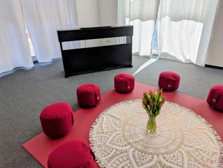 Fünf bordeauxrote Meditationskissen im Kreis um ein rundes Mandala-Tuch mit Tulpen, dahinter ein E-Piano